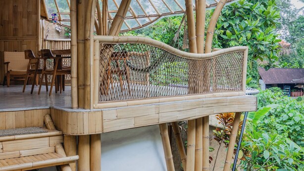 Una estructura de bambú con techo de paja, un banco de madera y una pequeña mesa con sillas.