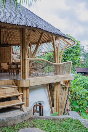 Une structure en bambou surmontée d’un toit de chaume, avec un banc en bois et une petite table entourée de chaises.