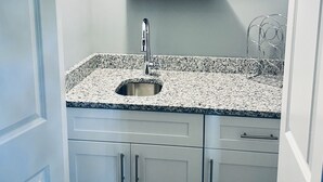Una cucina con piano di lavoro in granito, lavello in acciaio inox e pensili bianchi. Quattro bicchieri da vino si trovano su un ripiano sopra il lavello.