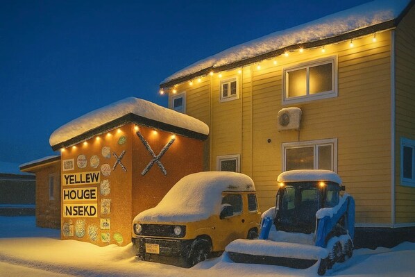A yellow house with a snow-covered roof and a sign reading "YELLOW HOUSE NSEKD". - Yellow House Niseko (Kutchan)
