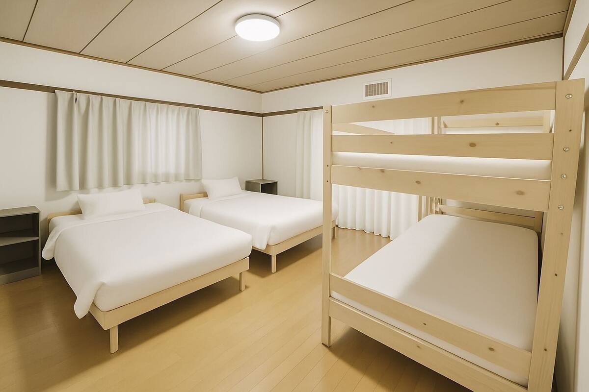 A hotel room with two single beds, a bunk bed, wooden flooring, and white bedding.