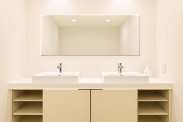 Een badkamer met twee wastafels, een grote spiegel en beige kastjes.