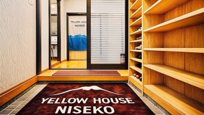 A hotel hallway with a wooden shoe rack, a blue towel, and a sign reading "YELLOW HOUSE NISEKO". - Yellow House Niseko (Kutchan)