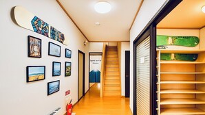 A hallway with framed pictures on the wall, a wooden staircase, and a green skateboard on a shelf. - Yellow House Niseko (Kutchan)