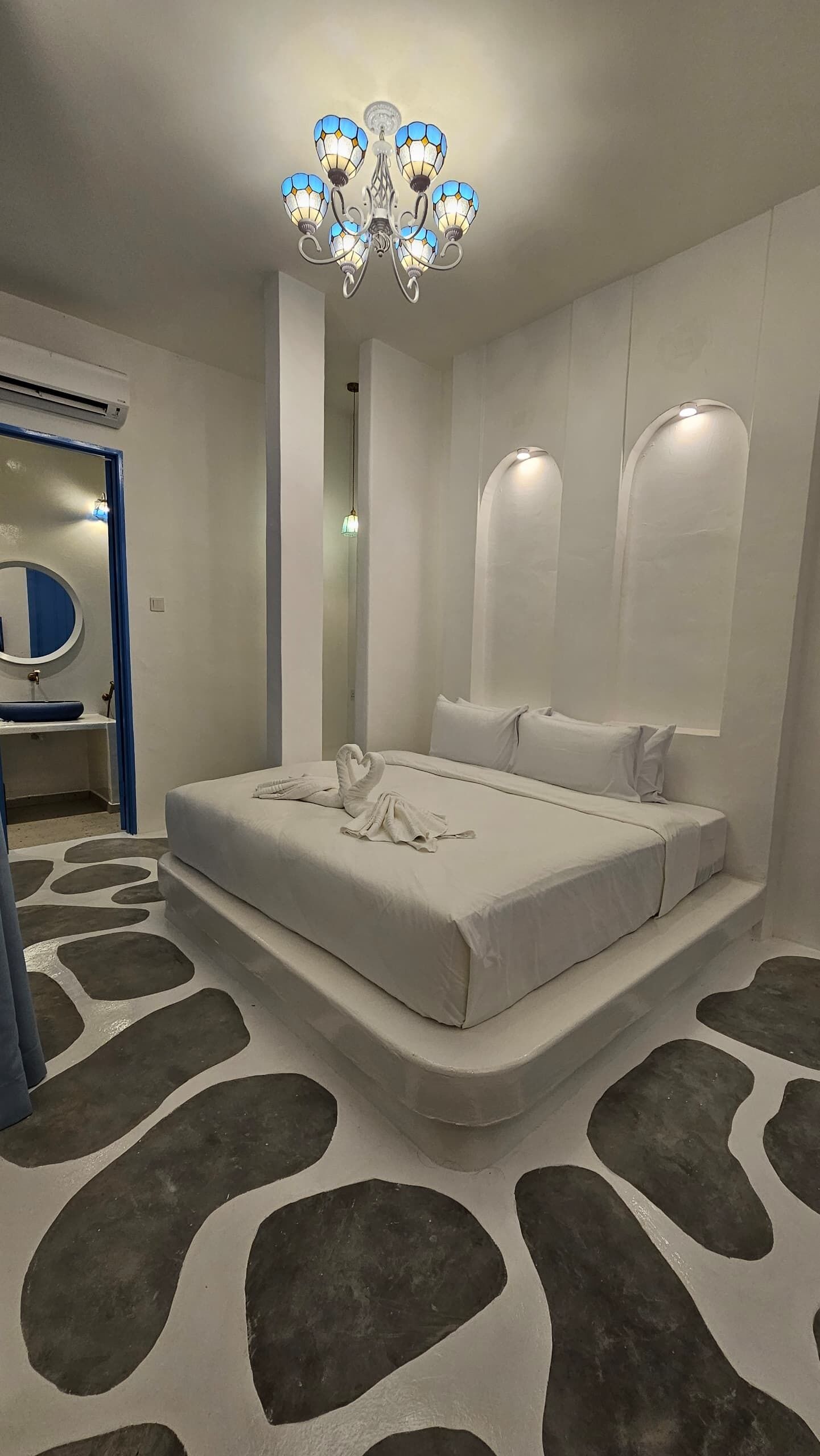 A modern bedroom with a large bed, a chandelier, and a unique floor design.