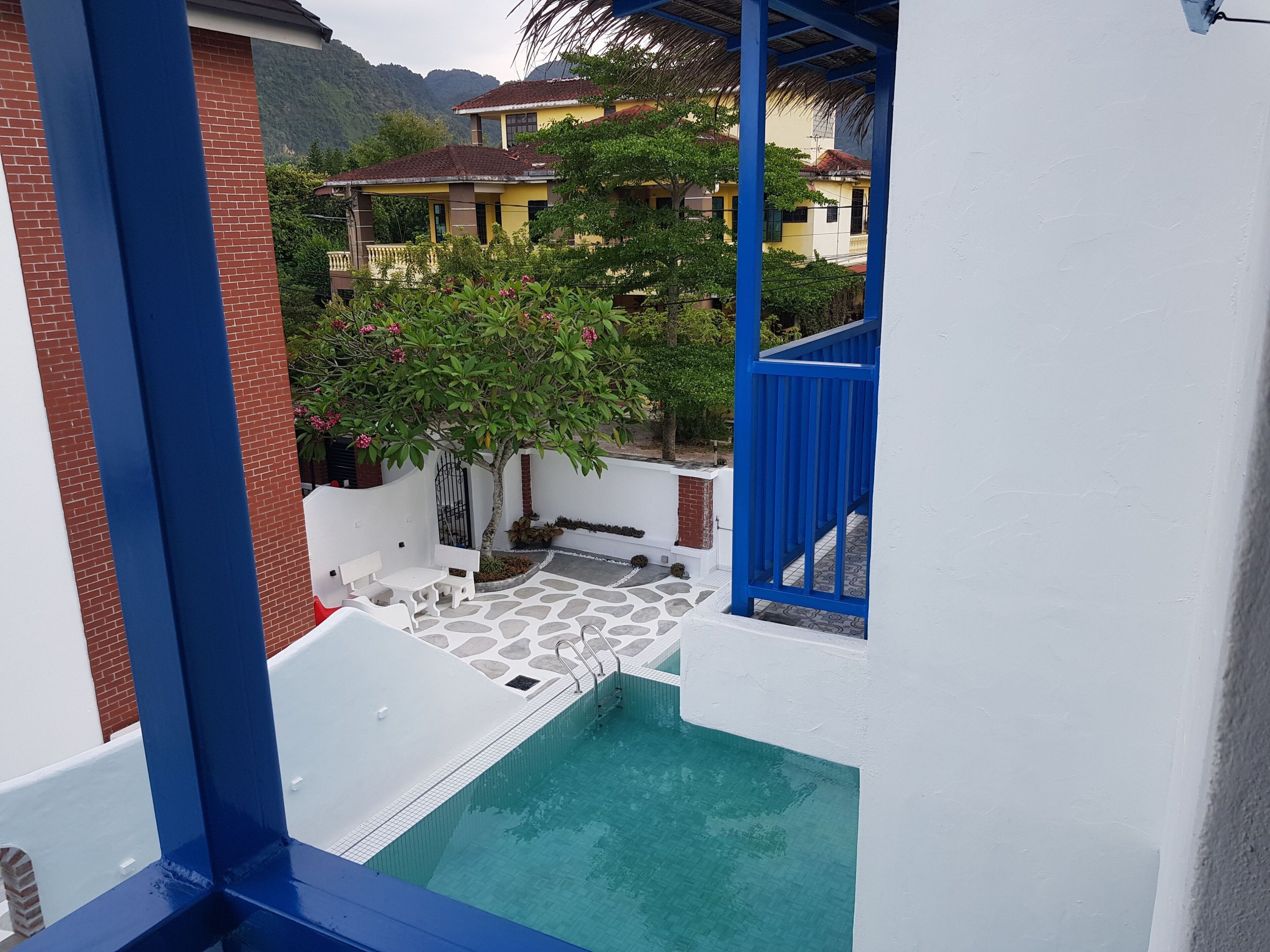 Un área de piscina con suelo de baldosas de piedra, un banco blanco y un árbol con flores rosadas.