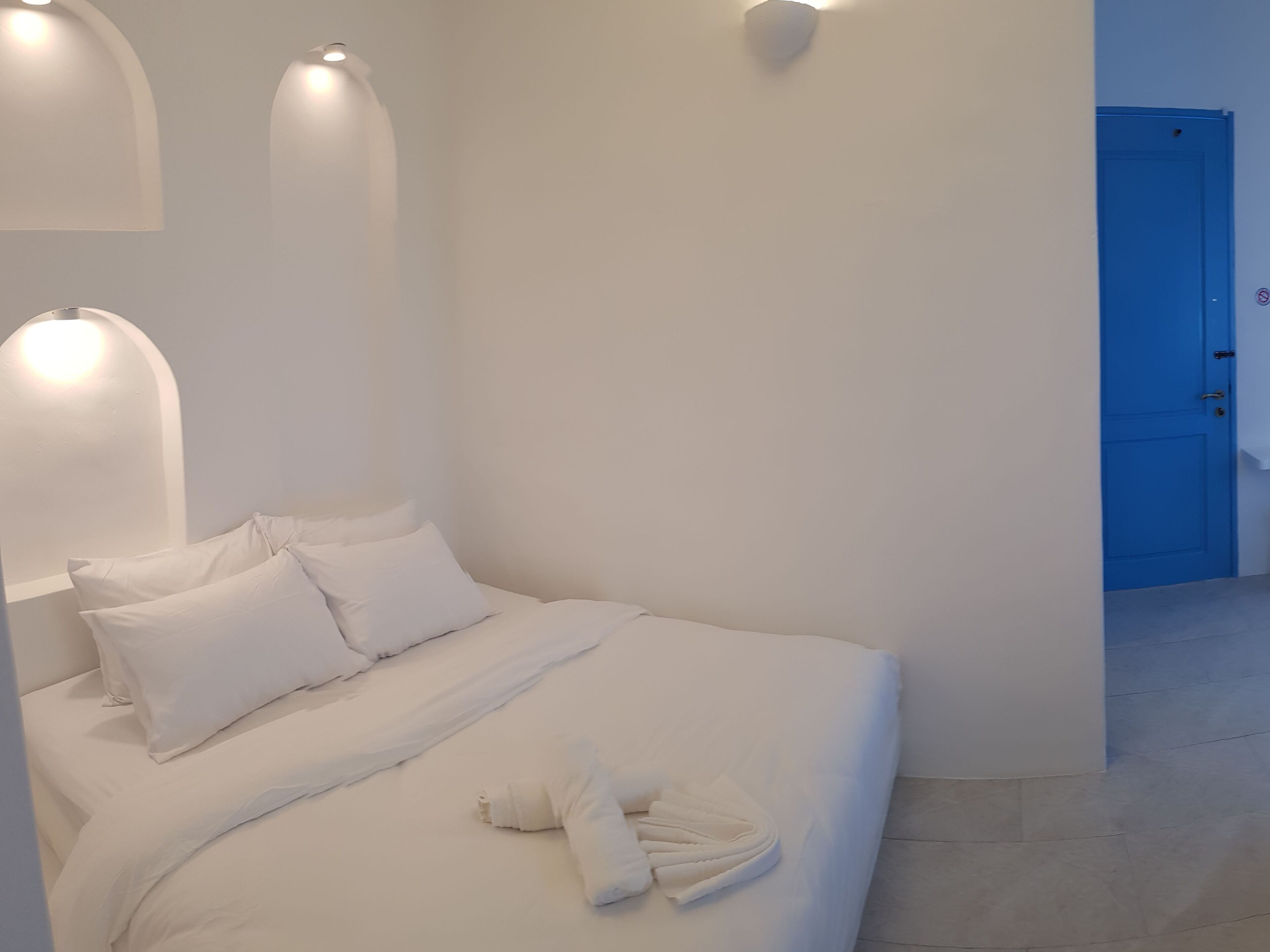 A neatly made bed with white linens and pillows, a blue door in the background, and a towel on the bed.