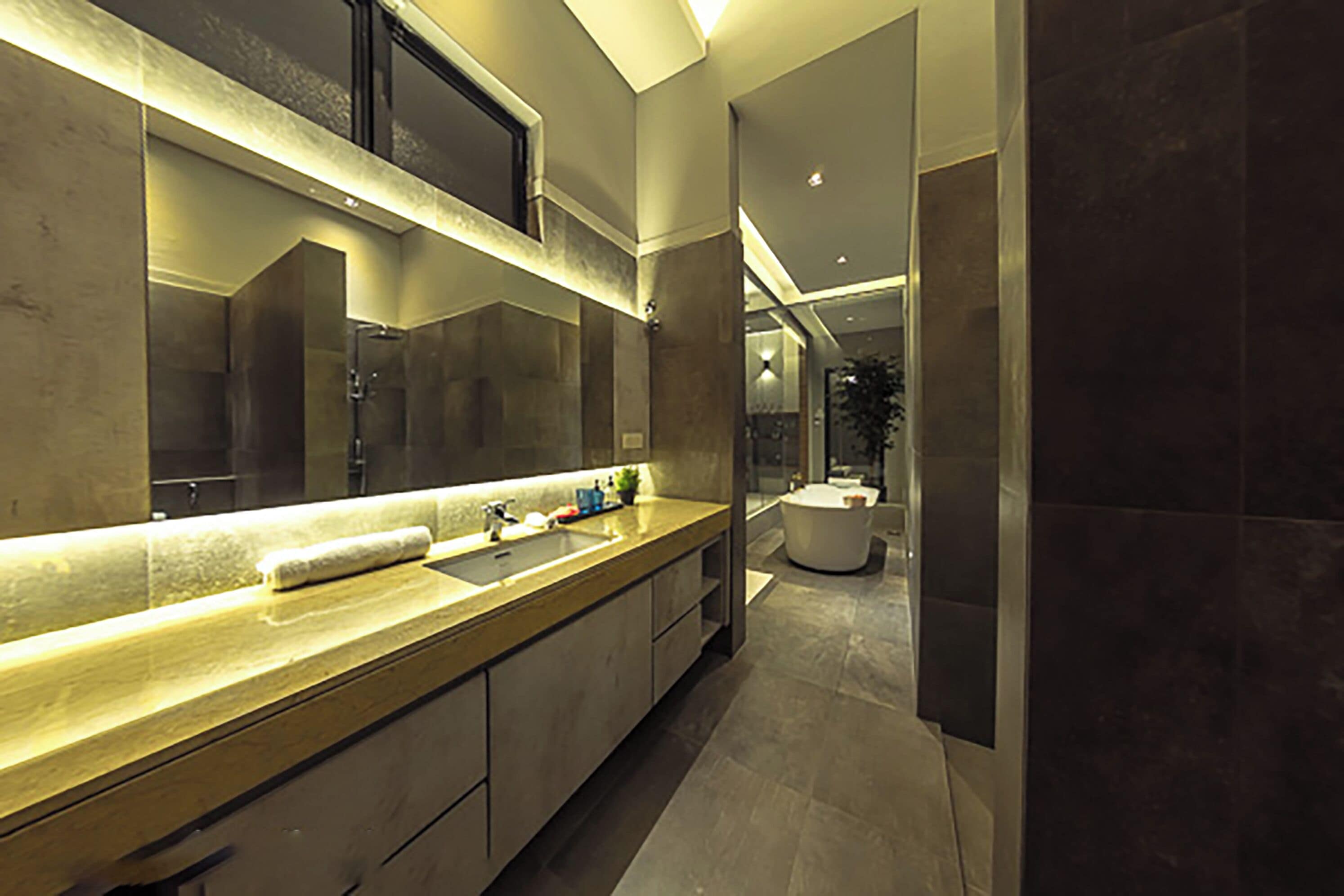 A modern bathroom with a long countertop, a large mirror, and a separate sink area.