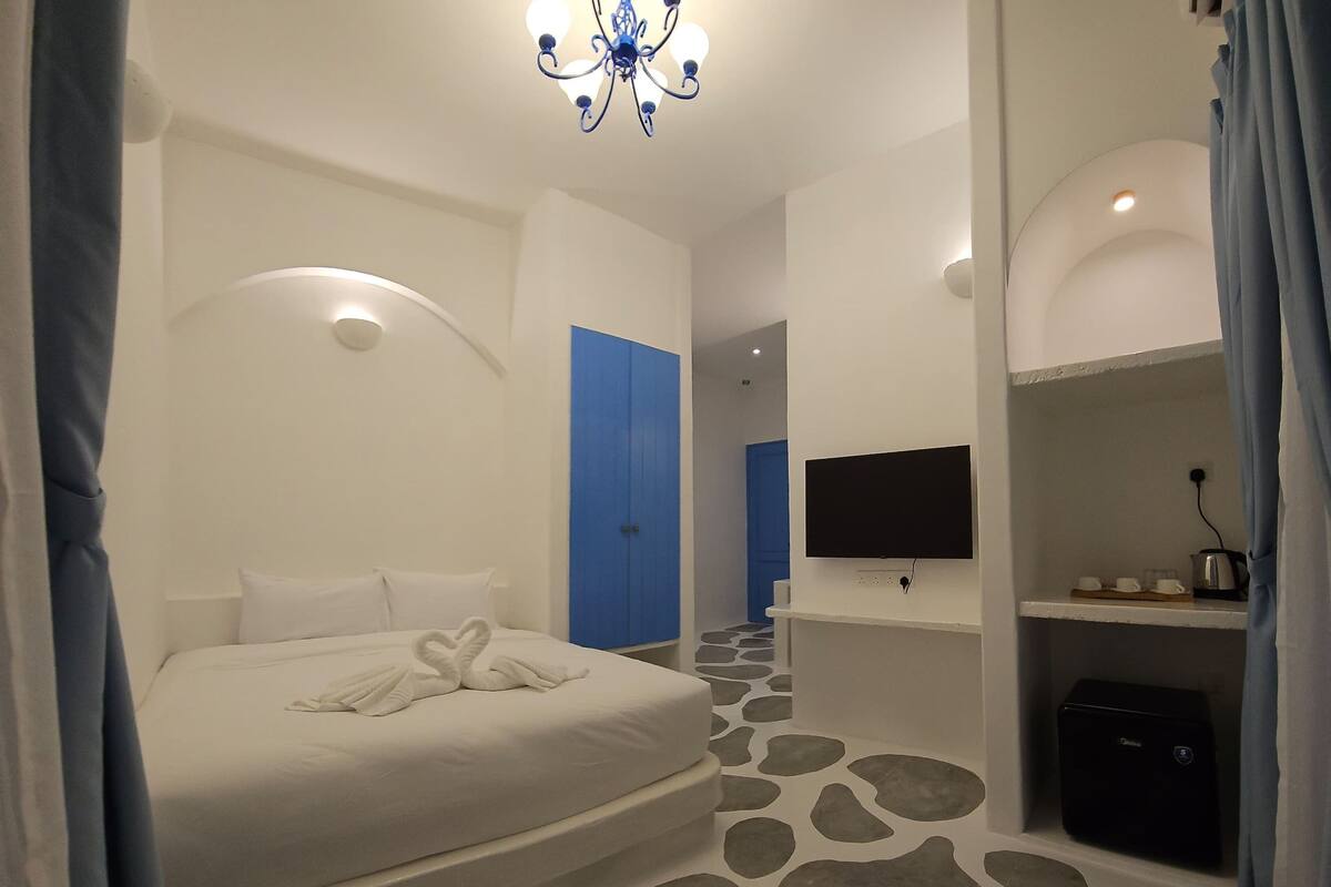 Ein modernes Hotelzimmer mit einem großen Bett, einem Flachbildfernseher, einer Minibar und einem Boden mit Steinmuster.