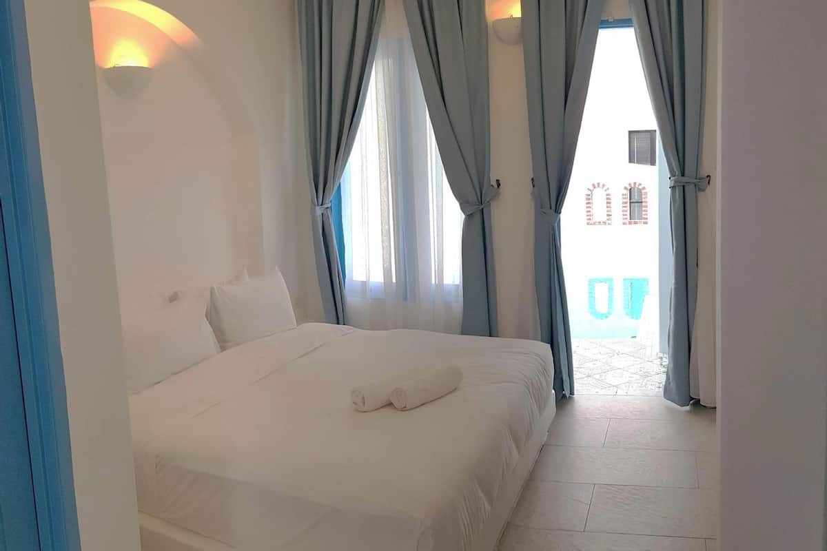 Ein Hotelzimmer mit einem großen Bett, weißen Leinen und hellblauen Vorhängen.