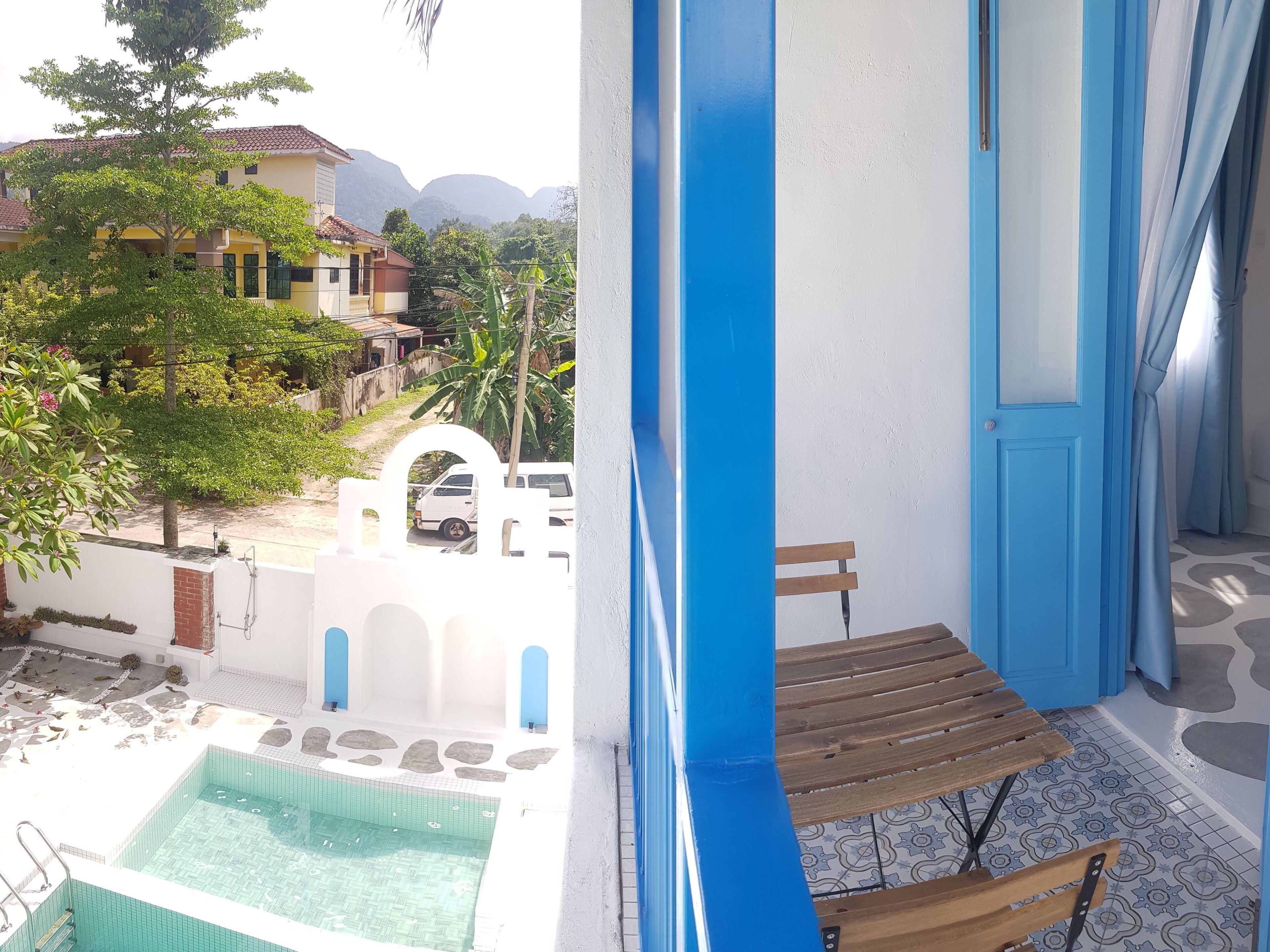 A balcony with a view of a swimming pool, a wooden bench, and a white wall with a blue door.