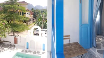 A balcony with a view of a swimming pool, a wooden bench, and a white wall with a blue door.