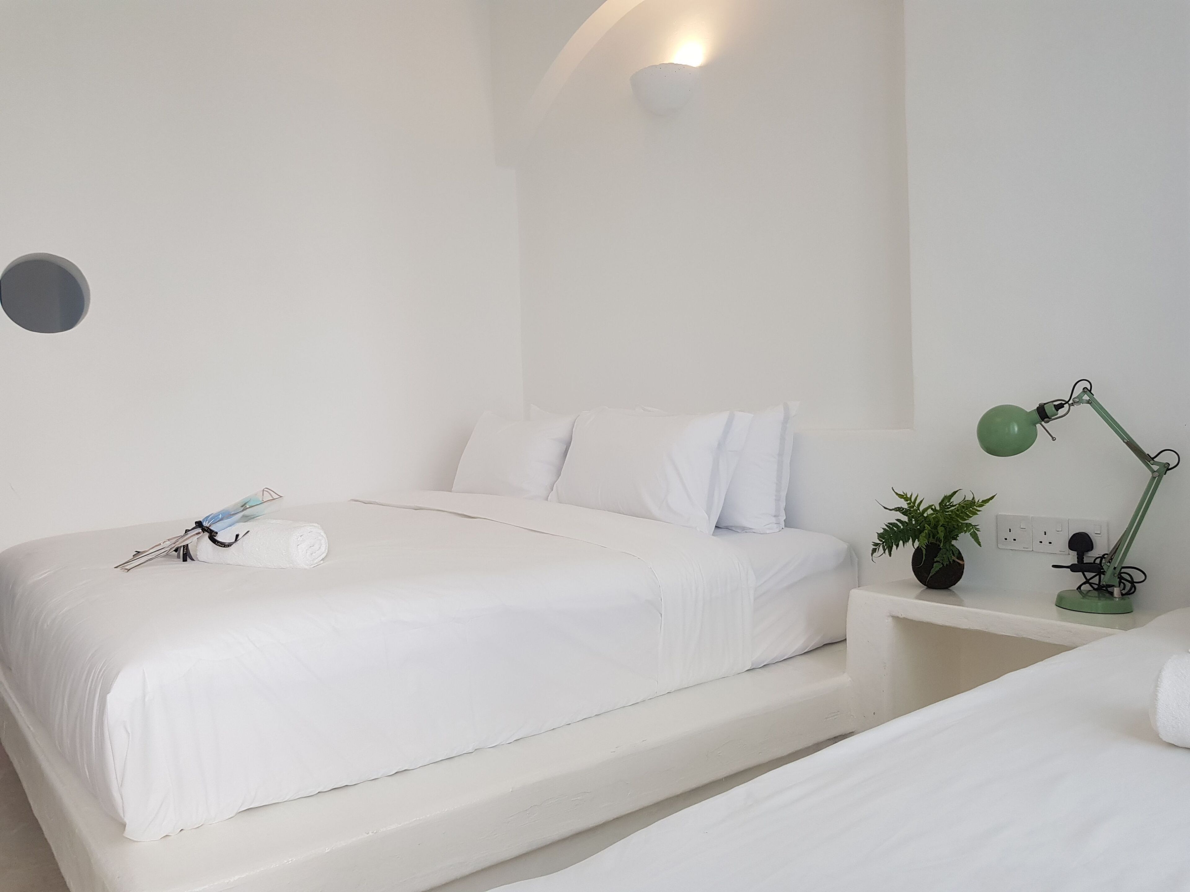 Camera da letto bianca e minimalista con letto, comodino, lampada e faretto a parete.