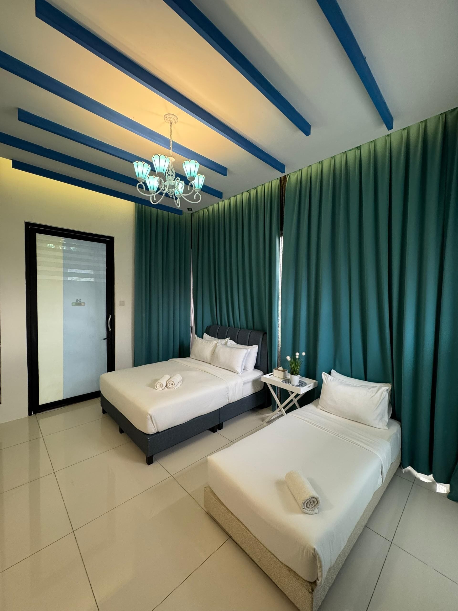 Habitación de hotel con dos camas, una araña, cortinas verdes y suelo de baldosas.