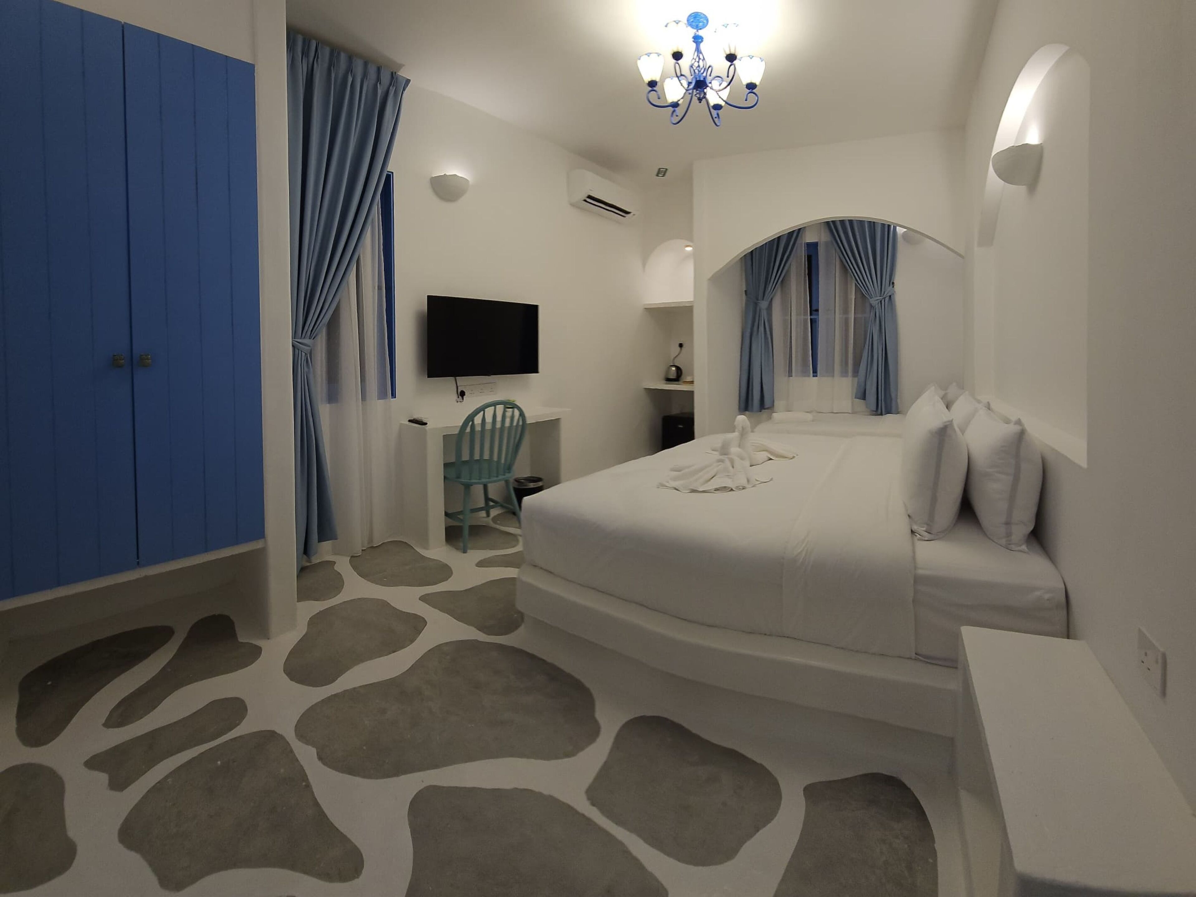 Habitación de hotel con cama, escritorio, silla, televisor y candelabro.