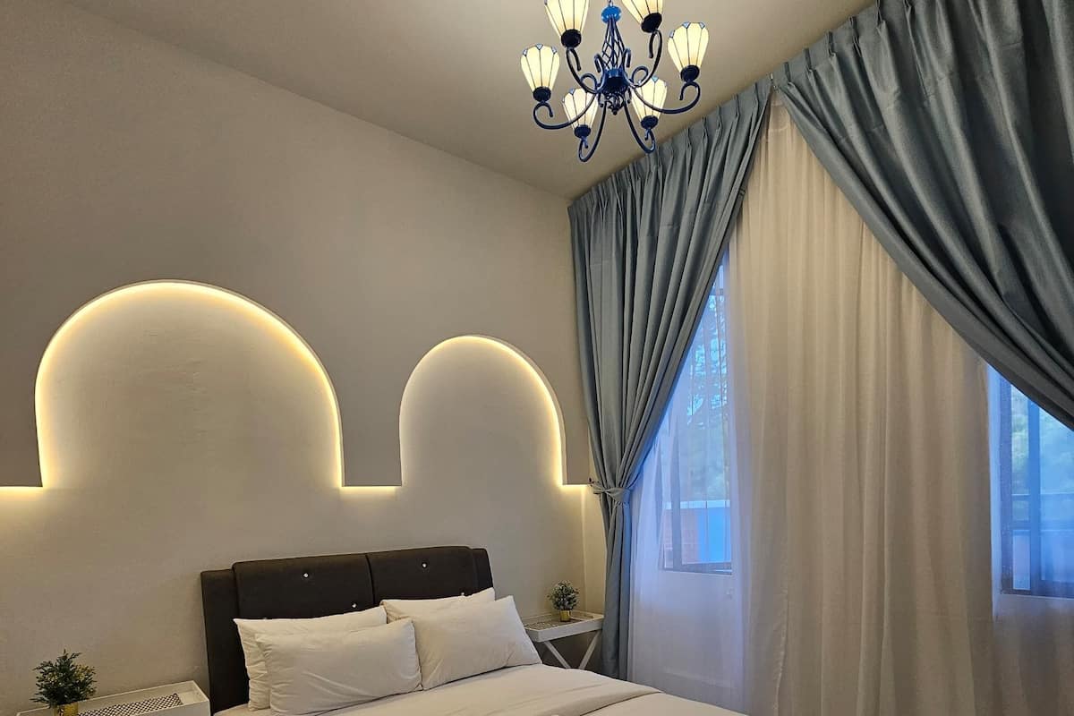 Ein modernes Schlafzimmer mit Bett, Nachttischen, einer Chandelierleuchte und einem Fenster mit Vorhängen.