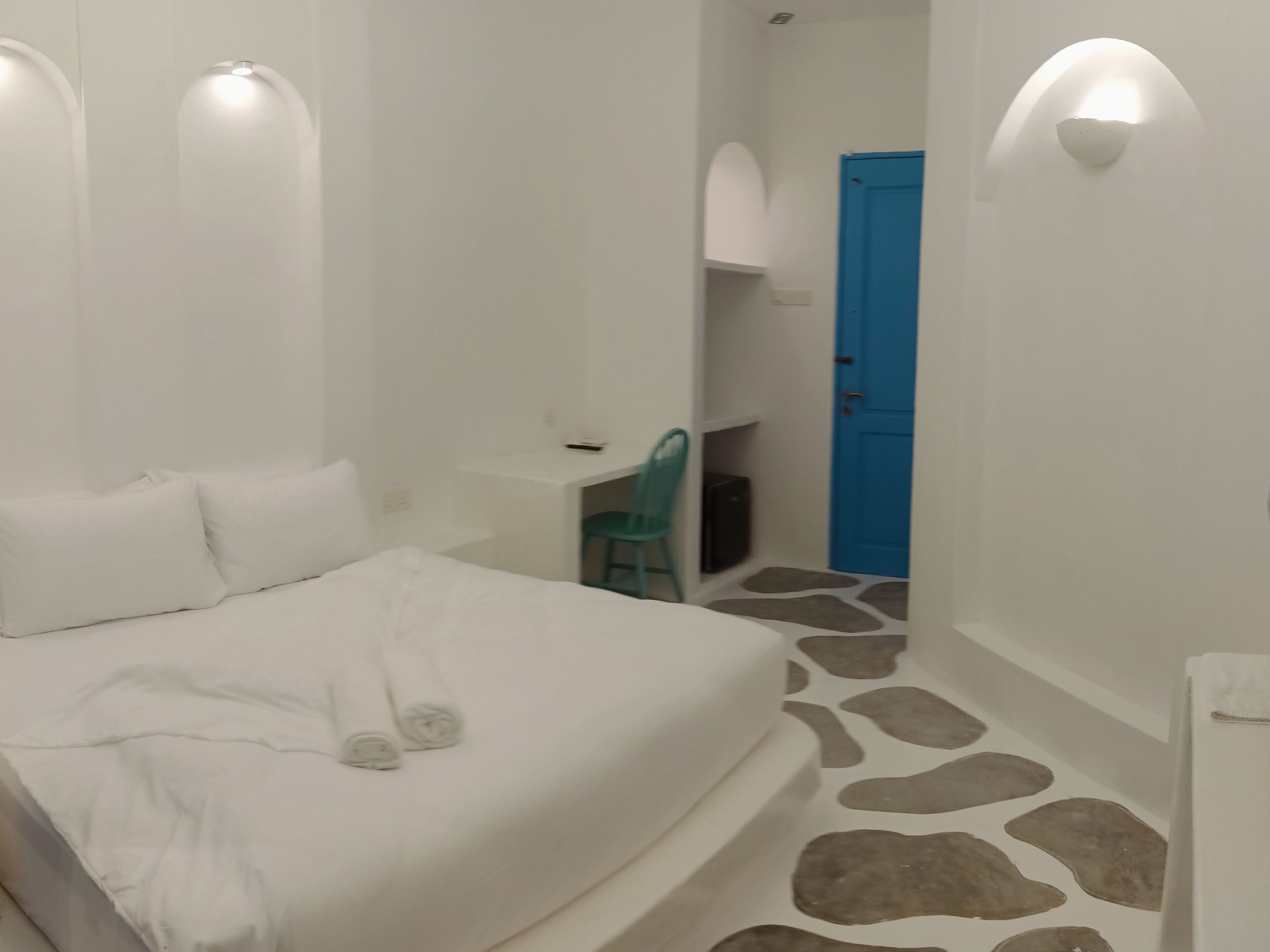 A bedroom with a bed, a desk, a chair, and a blue door.