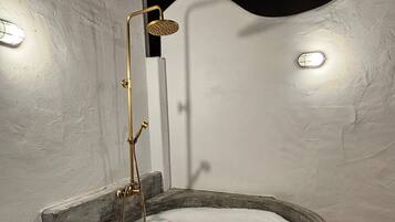 A circular hot tub with a showerhead, surrounded by stone steps and a white wall.