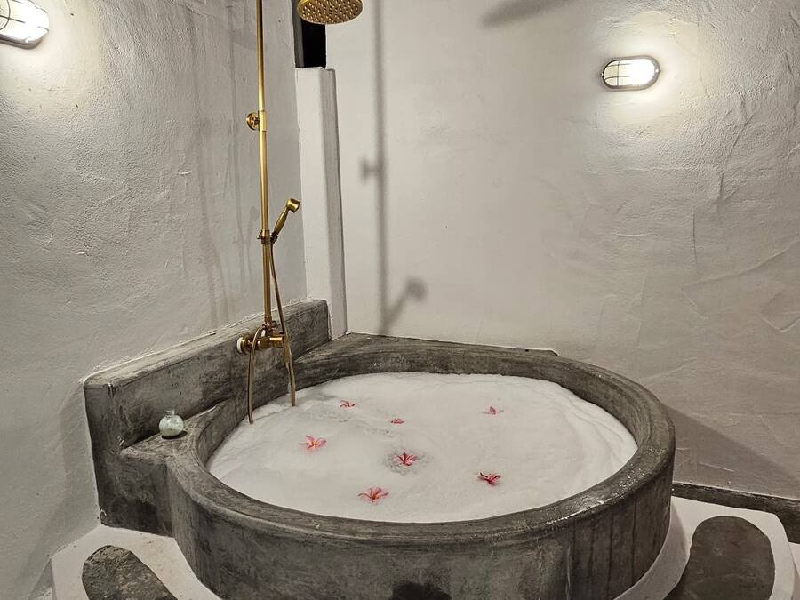 A circular hot tub with a showerhead, surrounded by stone steps and a white wall.