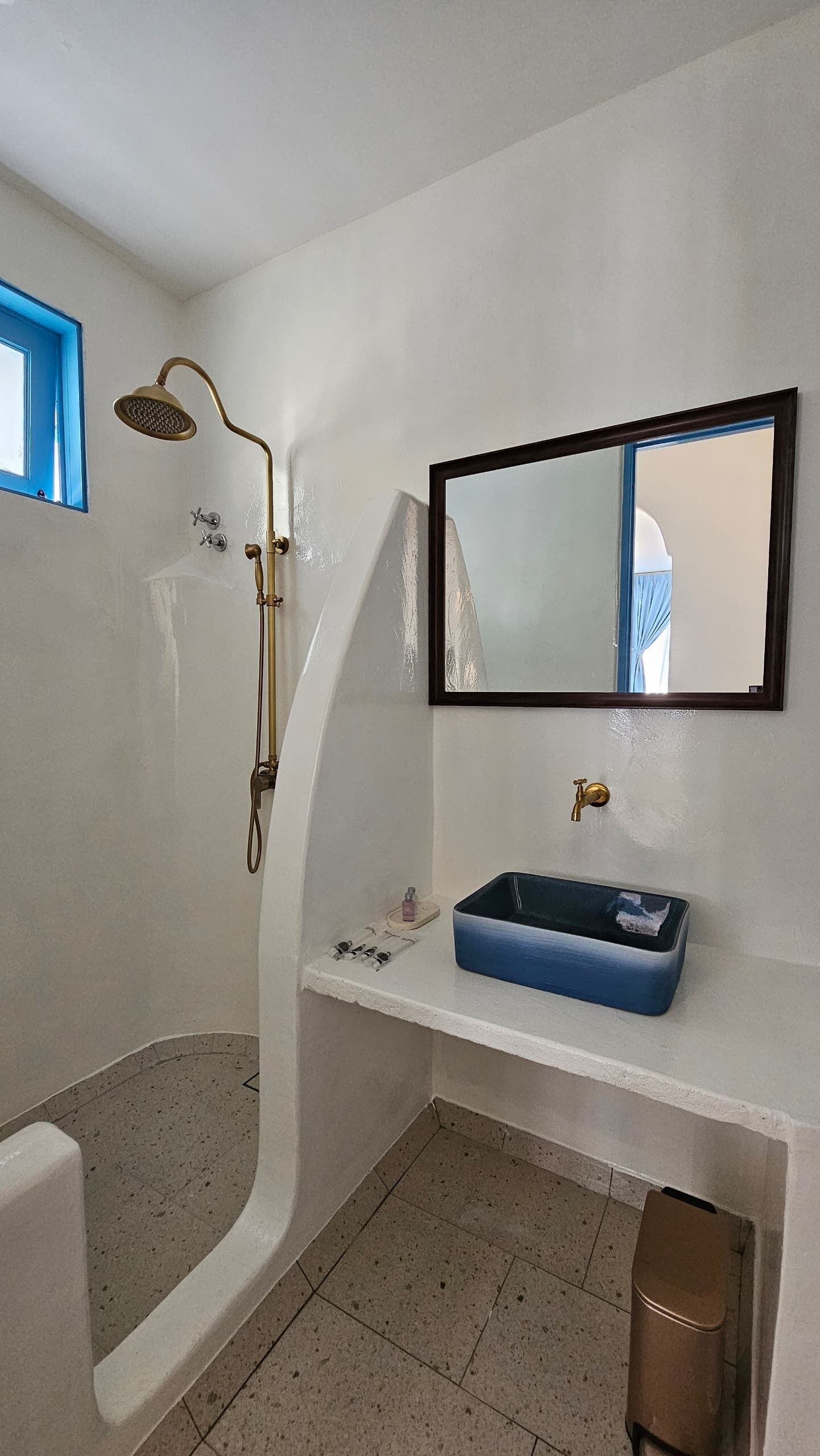 Un baño con una bañera independiente, un lavabo con lavamanos azul y una ducha con cabezal dorado.
