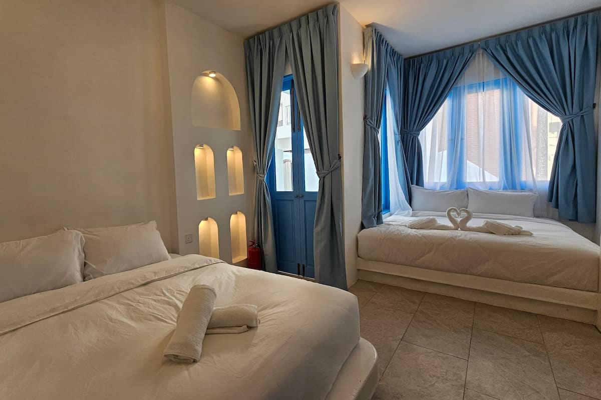 Ein Hotelzimmer mit zwei Betten, einer Wandleuchte und einem Fenster mit blauen Vorhängen.