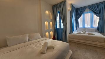 Una habitación de hotel con dos camas, una lámpara fijada a la pared y una ventana con cortinas azules.