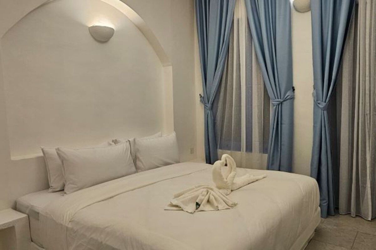 Camera d'albergo con un letto grande, biancheria da letto bianca e una testiera con una lampada.