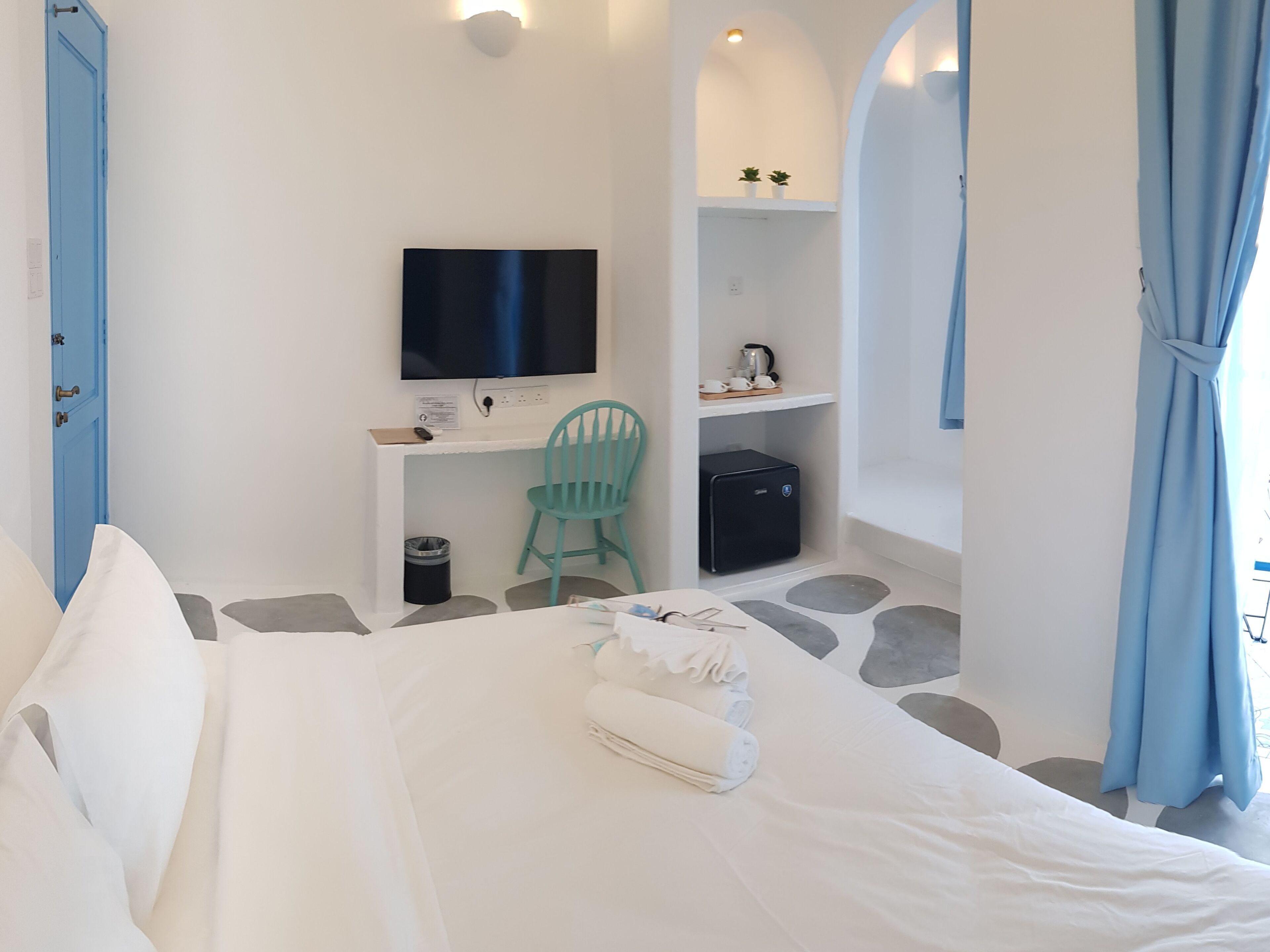 Quarto com cama, escrivaninha, cadeira, televisão e um pequeno armário.