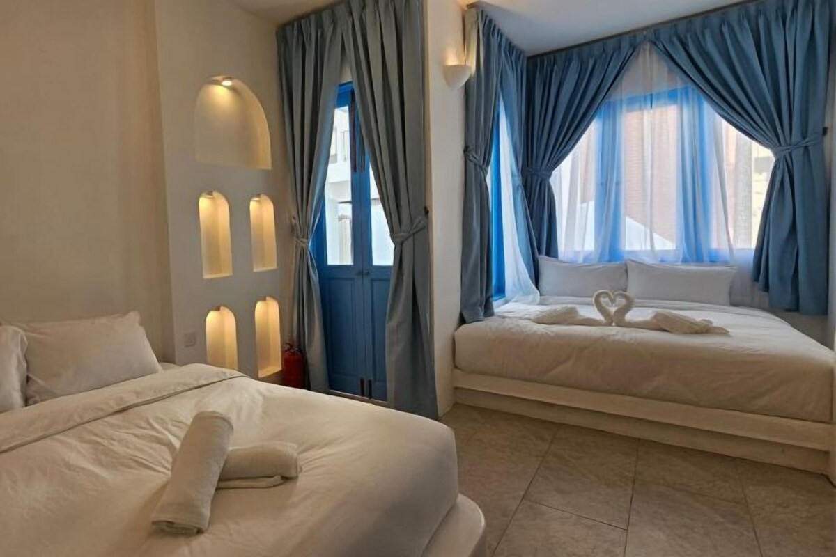 Ein Hotelzimmer mit zwei Betten, einer Wandleuchte und Blick auf die Stadt.