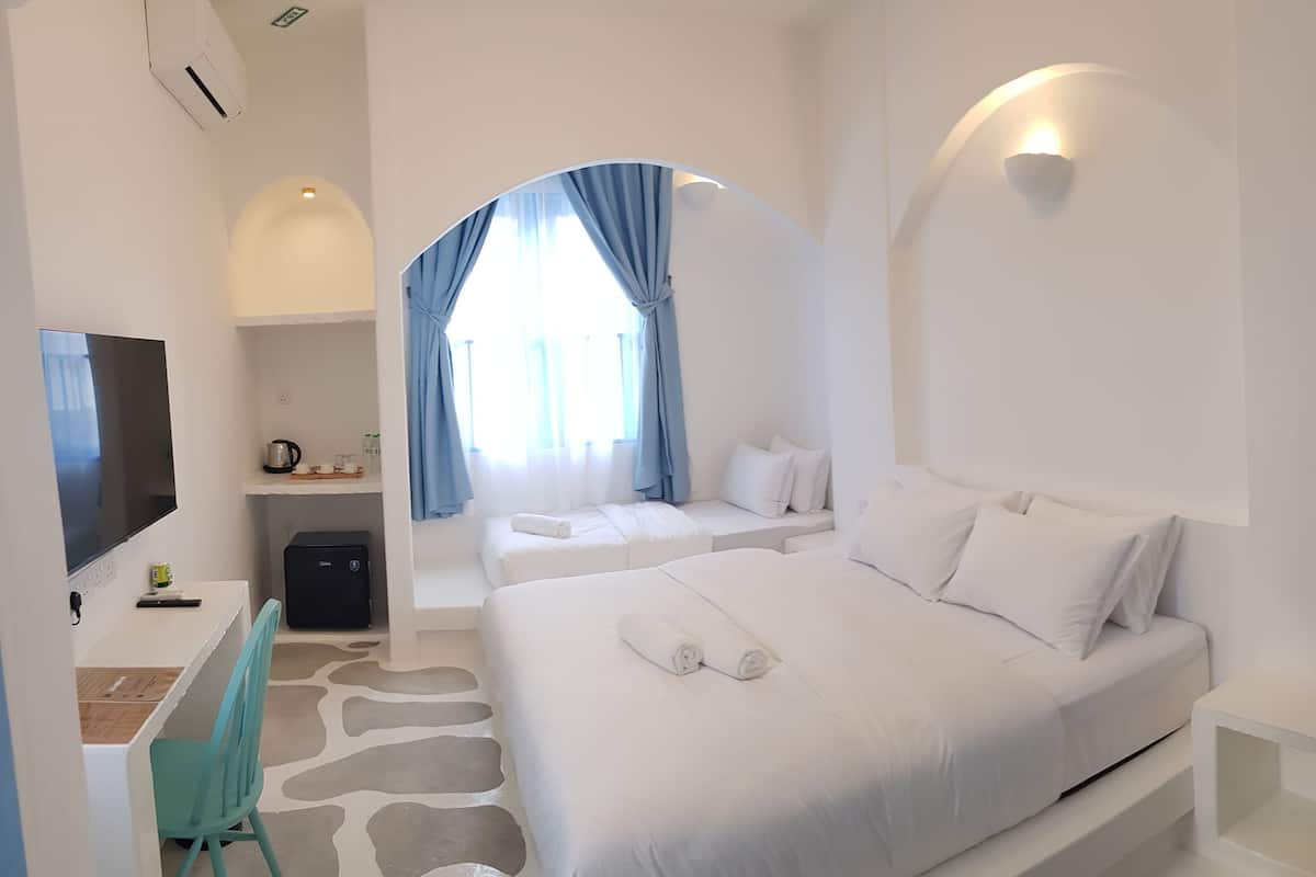 Ein modernes Hotelzimmer mit einem großen Bett, einem Schreibtisch mit Stuhl, einem Flachbildfernseher und einer kleinen Küchenzeile.