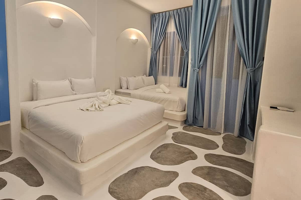 Ein modernes Hotelzimmer mit zwei Betten, einem fußbodenähnlichen Steinmuster und blauen Vorhängen.