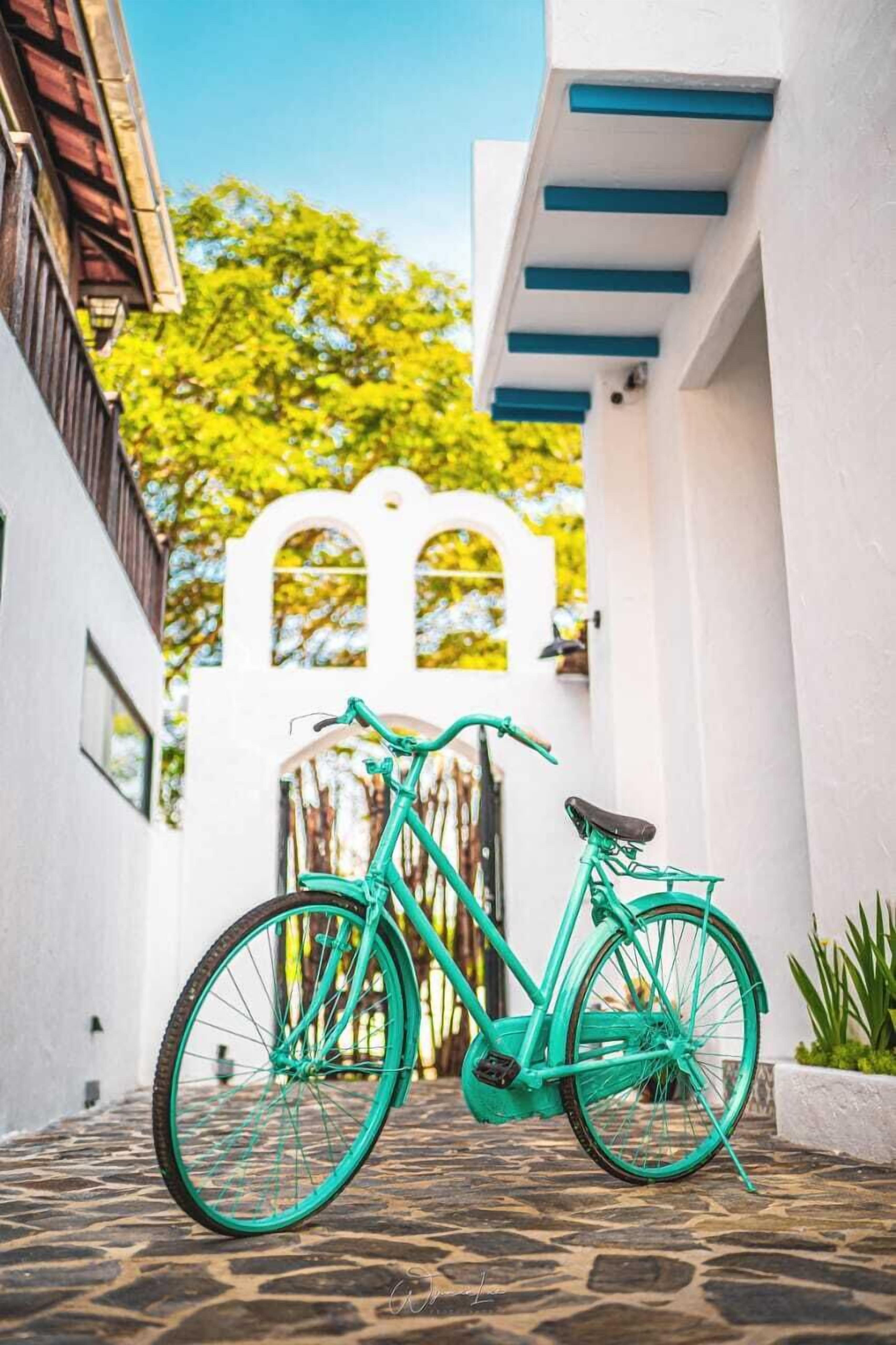 A turquoise bicycle parked in a narrow alleyway with a white building and a decorative archway in the background.