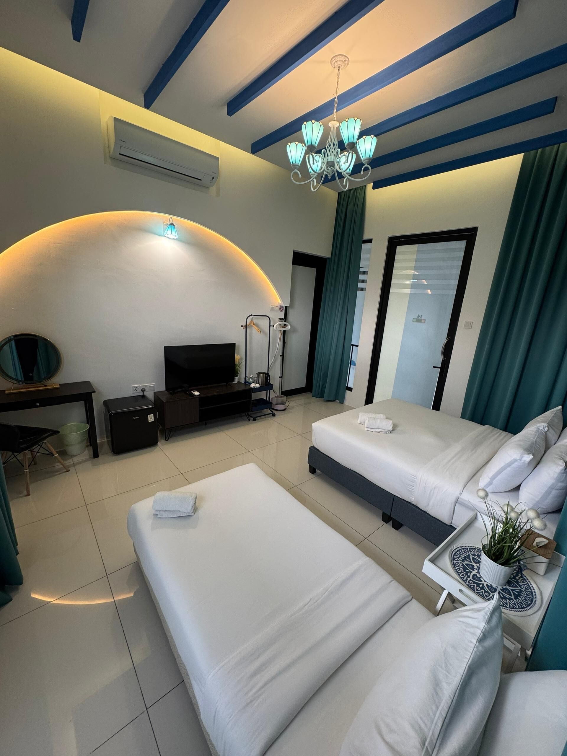 A hotel room with two beds, a TV, a desk, and a shower area.