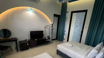 A hotel room with two beds, a TV, a desk, and a shower area.