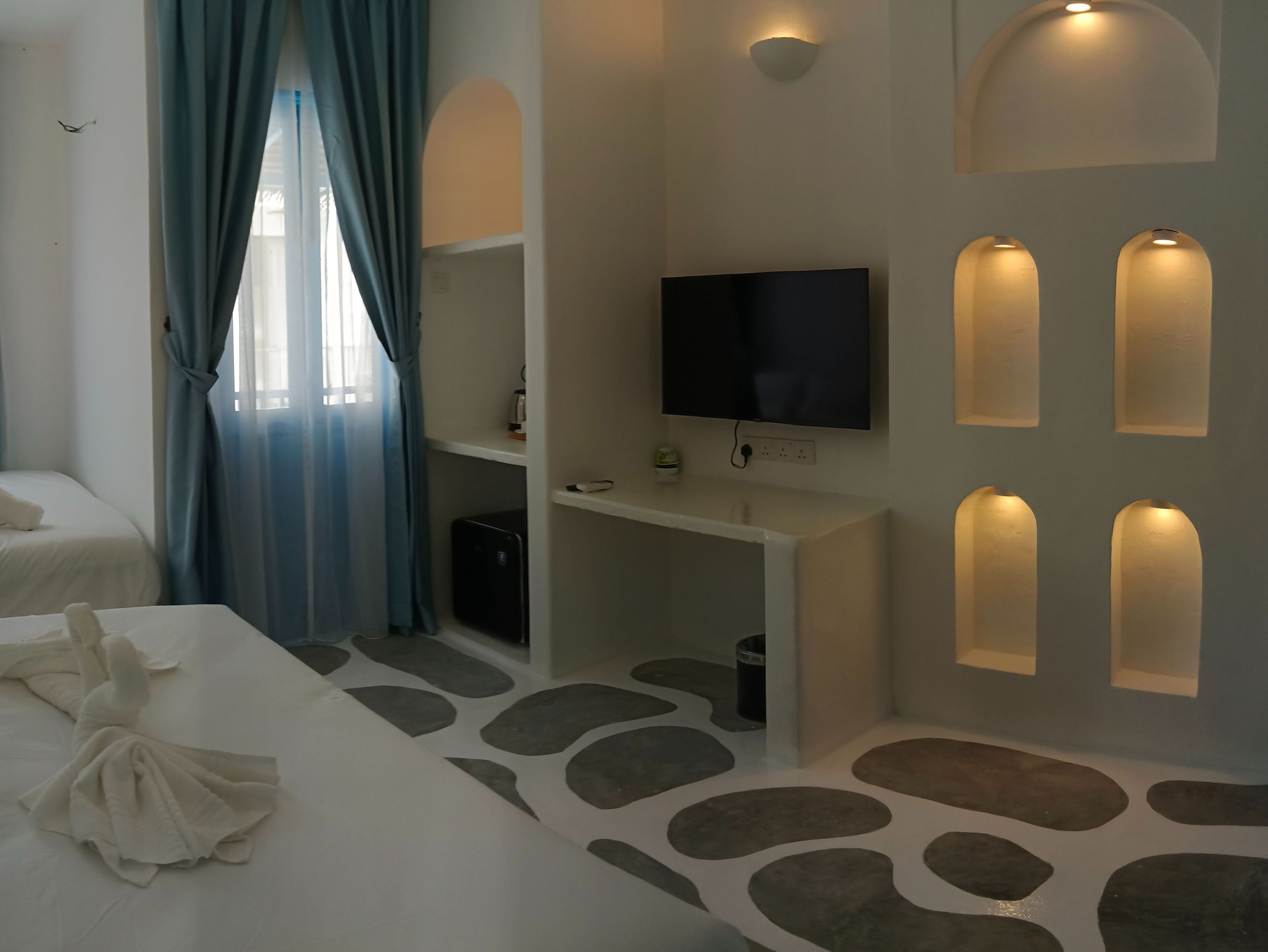 A hotel room with a bed, a desk with a TV, and a wall with built-in lighting.