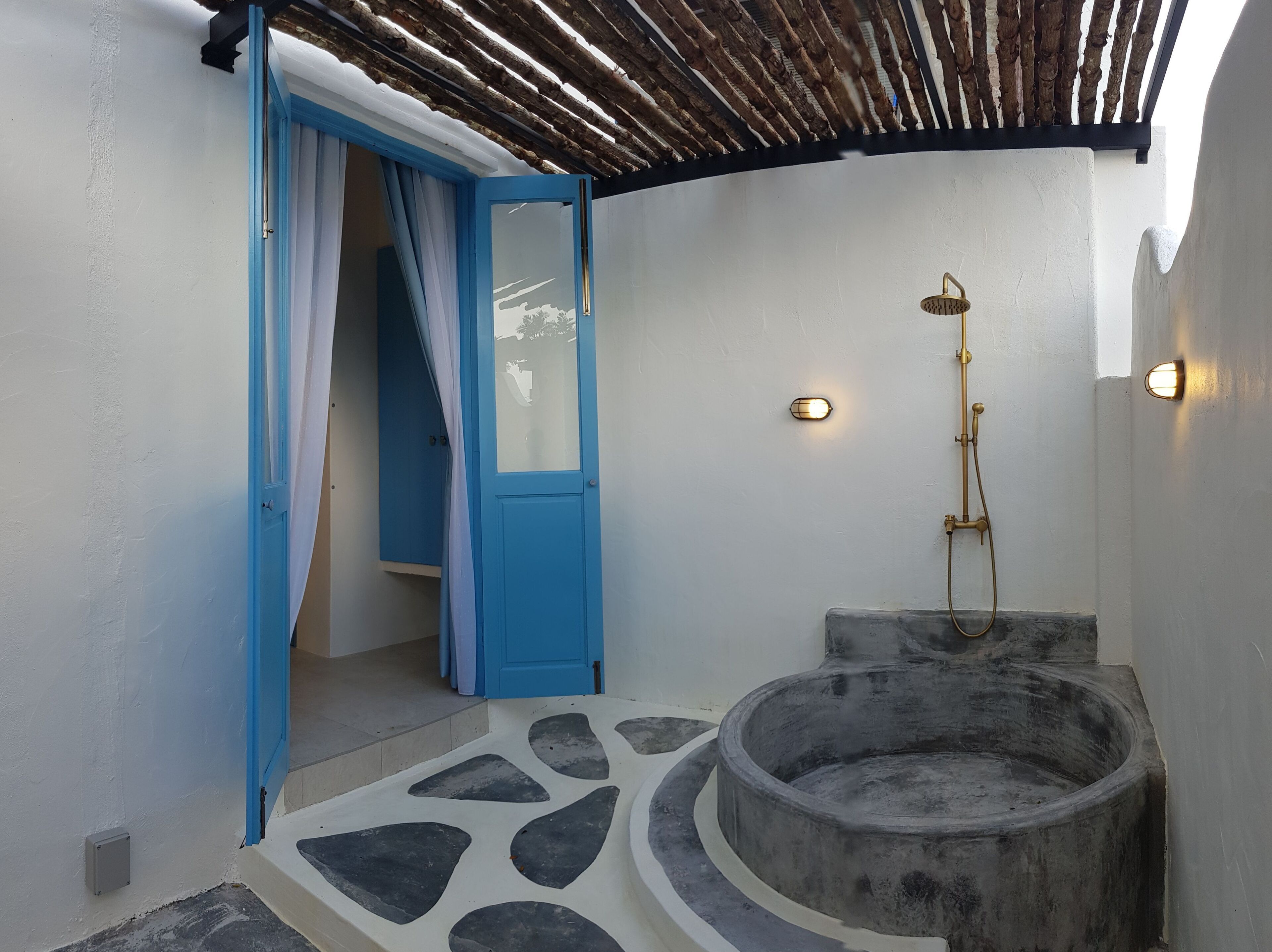 Un baño con una puerta azul, una ducha con cabezal dorado y un lavabo de piedra.