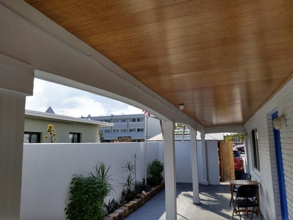 A covered outdoor area with a wooden ceiling, white walls, and a small table with chairs.
