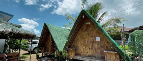 Two wooden huts with green roofs, surrounded by potted plants and a gravel path.