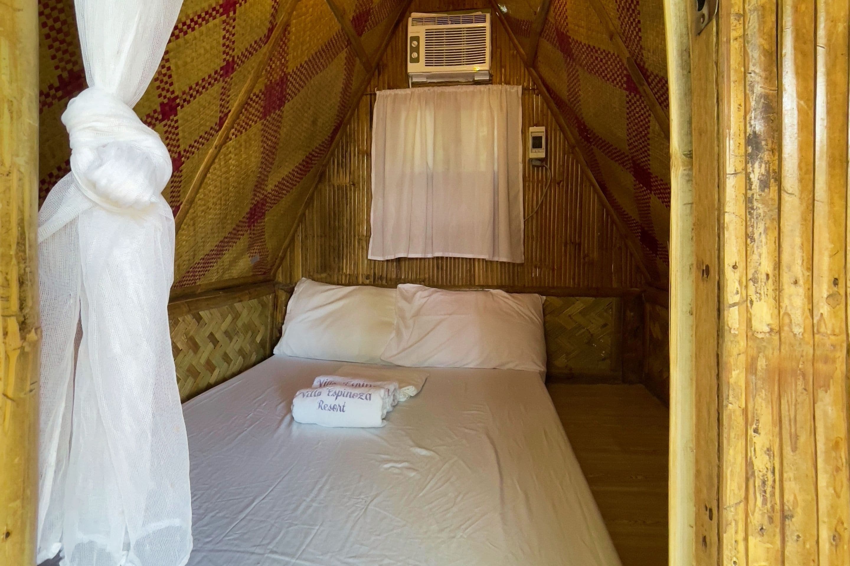 Eine gemütliche Einzelunterkunft mit einem Bett, einem Moskitonetz und einem Fenster mit Klimaanlage.