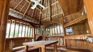 A wooden interior with a table and benches, a ceiling fan, and a window with a view of greenery.