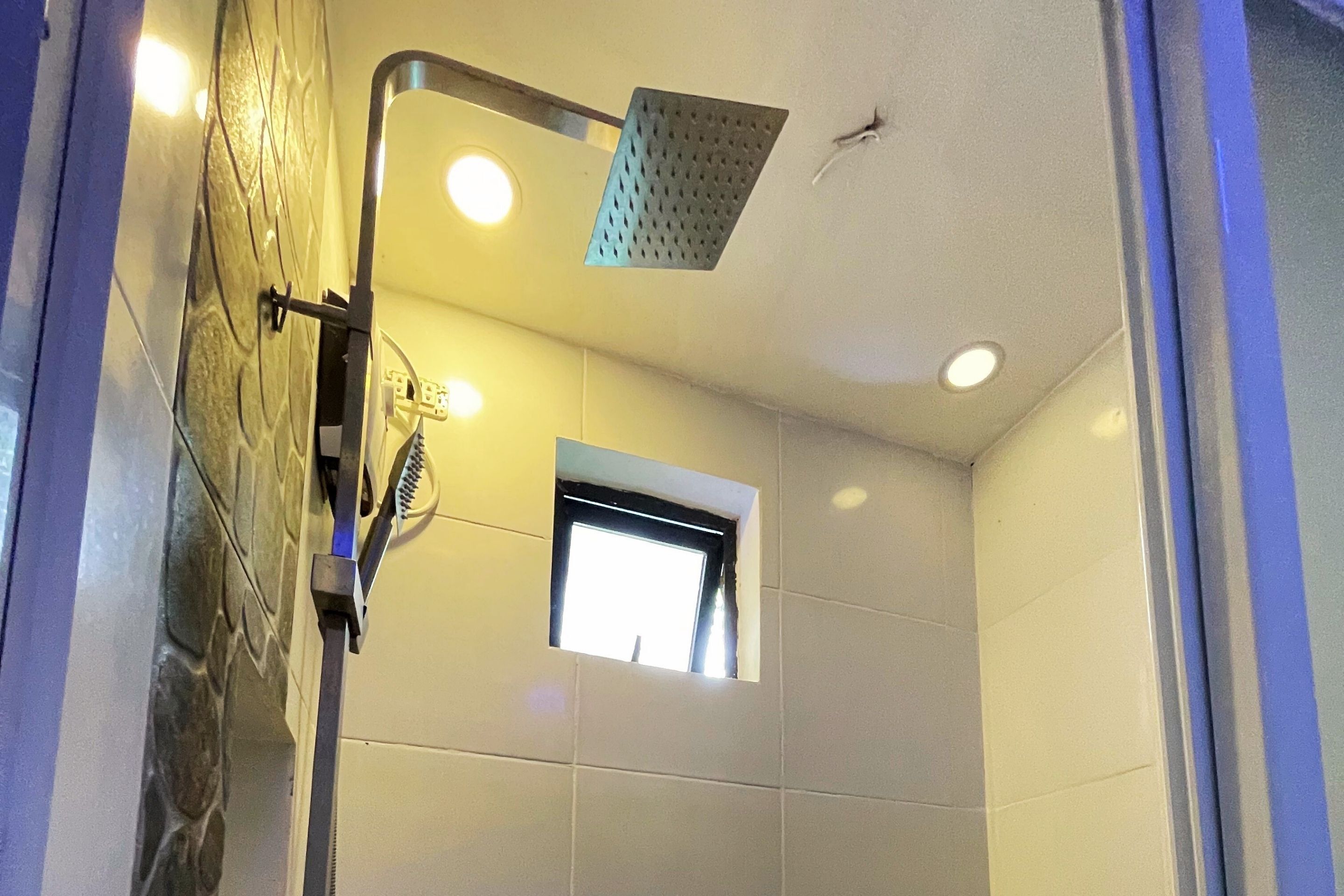 A shower with a handheld showerhead and a window above it.