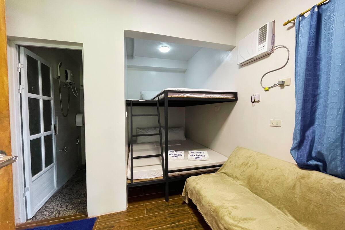 A dormitory room with bunk beds, a sofa, a shower, and an air conditioning unit.