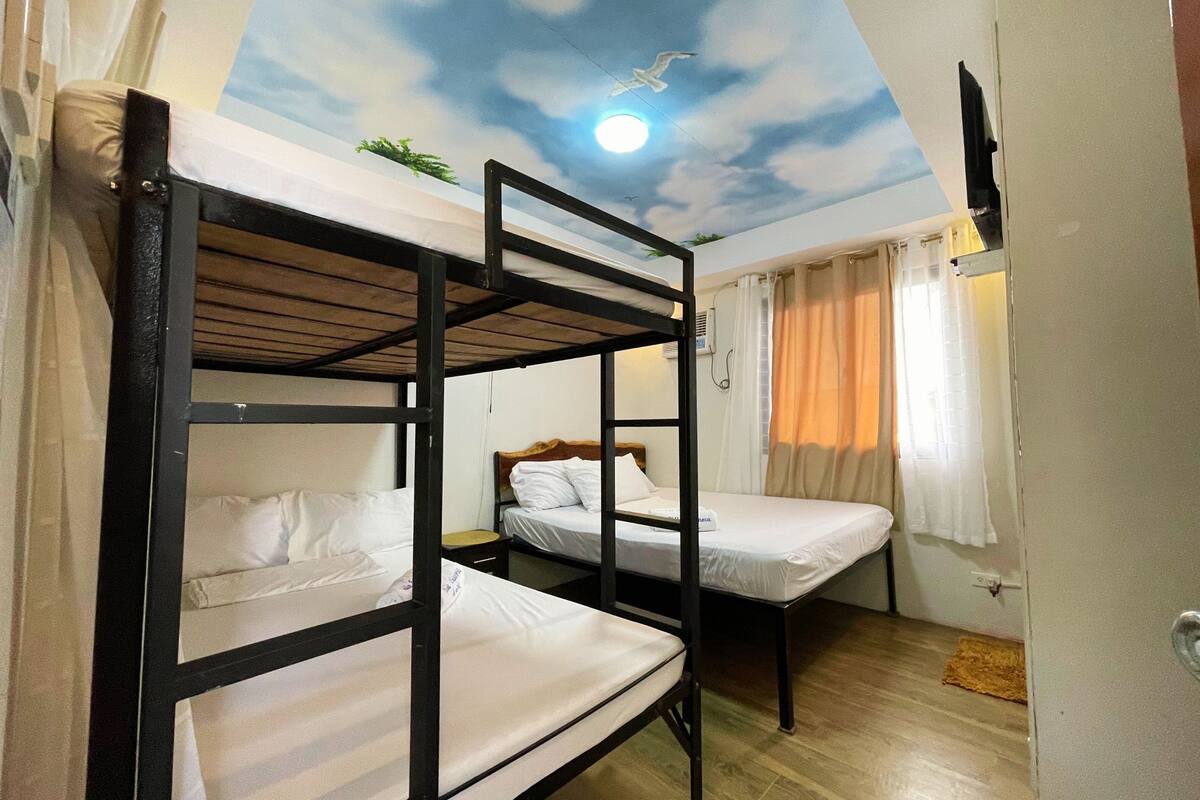 A room with bunk beds, a ceiling mural, and a window with curtains.