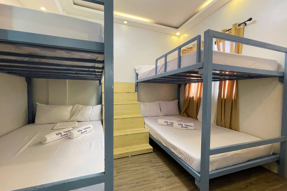 A room with bunk beds, a wooden staircase, and a bed with a rolled towel.