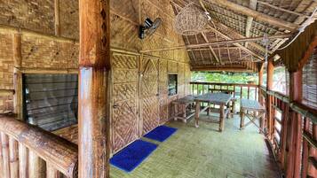 A bamboo-walled room with a thatched roof, a wooden table, and a blue mat on the floor.