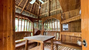 A wooden interior with a table and benches, a ceiling fan, and a view of greenery outside.