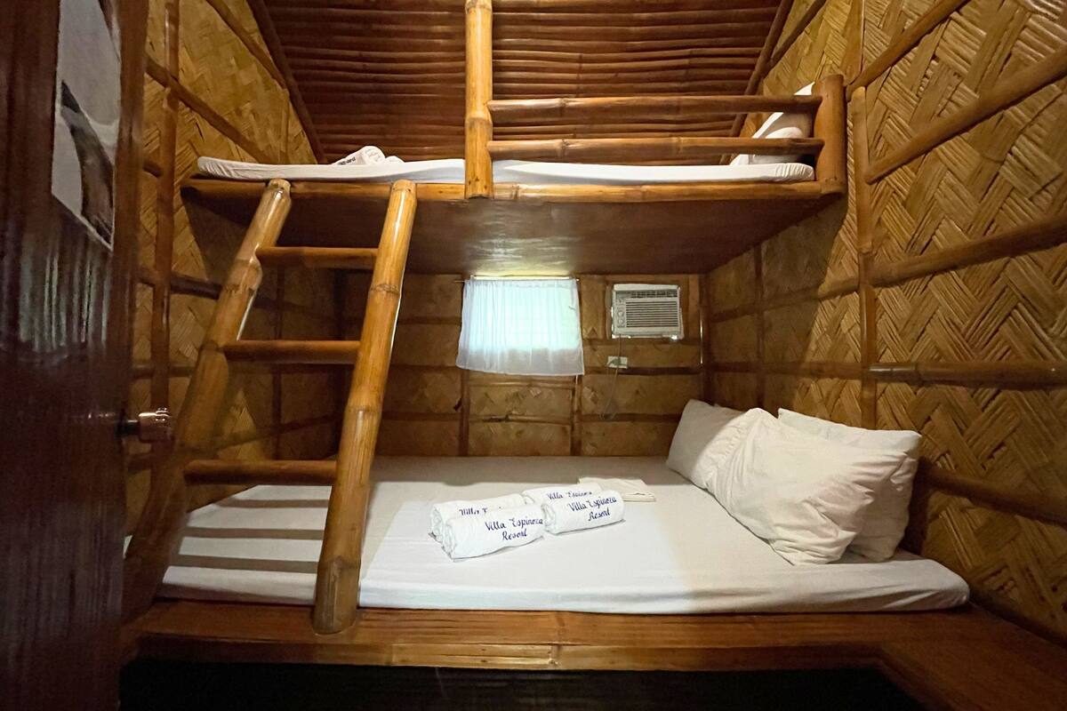 A bunk bed room with wooden walls and a ladder. There is a window with a curtain and an air conditioning unit on the wall.