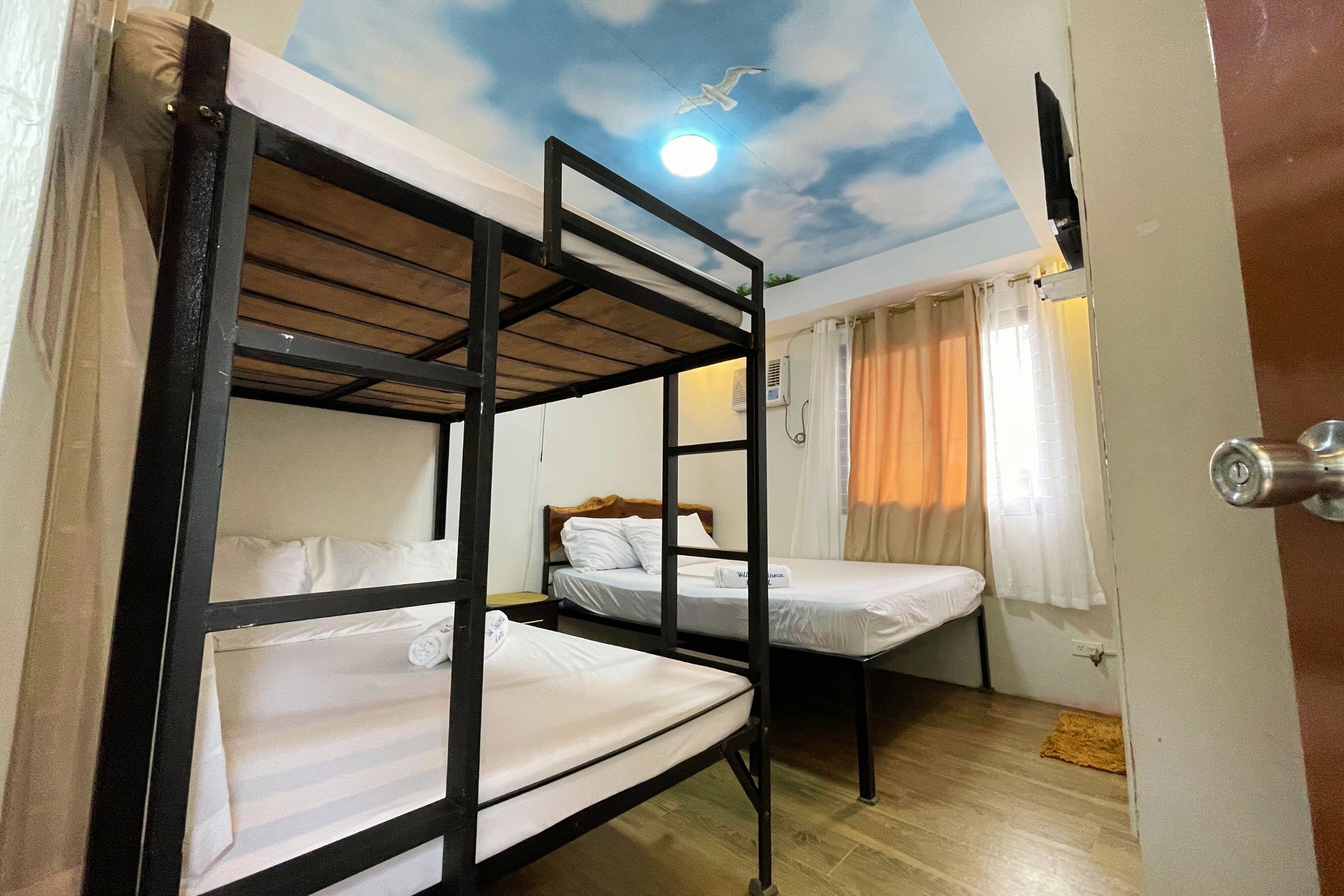 A dormitory room with bunk beds, a ceiling mural, and a door with a handle.
