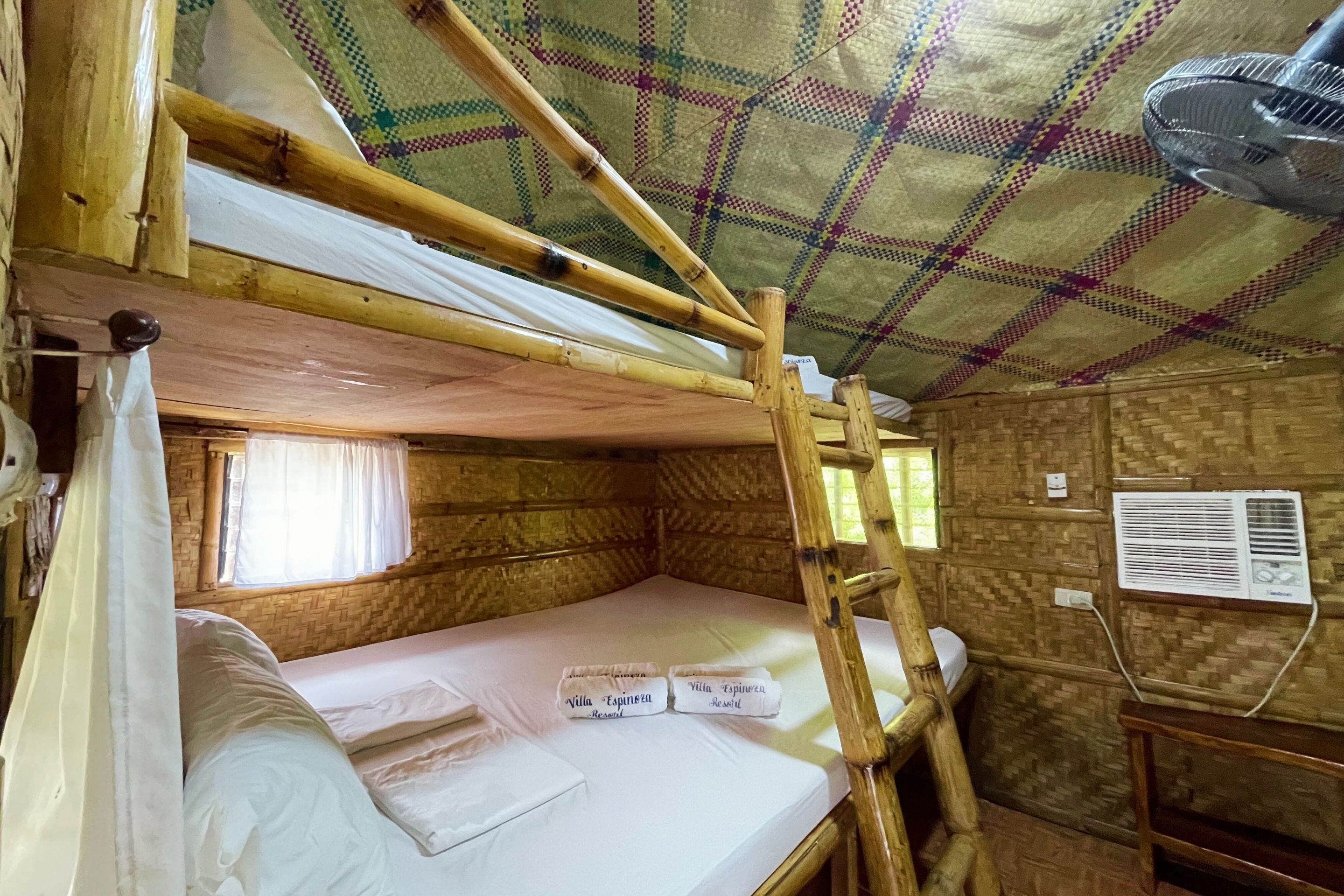 A rustic wooden room with a bunk bed, a fan, and a window with curtains.