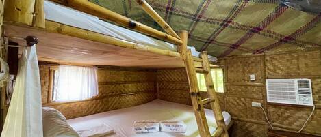 A rustic wooden room with a bunk bed, a fan, and a window with curtains.